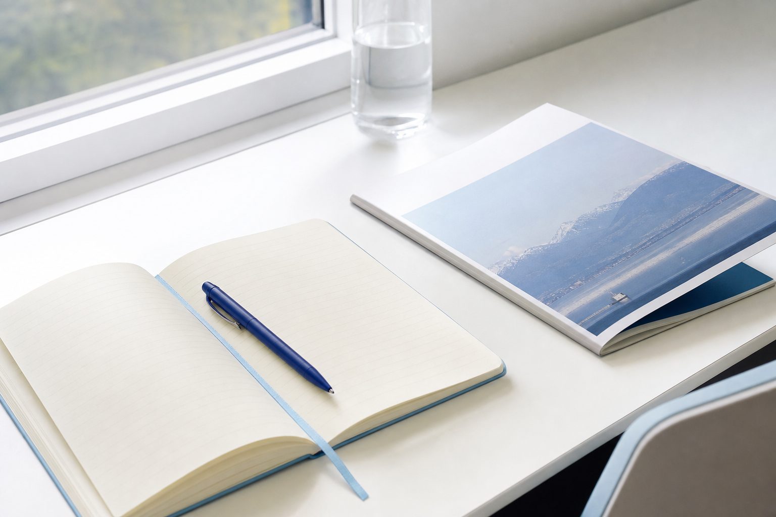Notebook and printed reference booklet on a sunlit white desk with an indigo pen